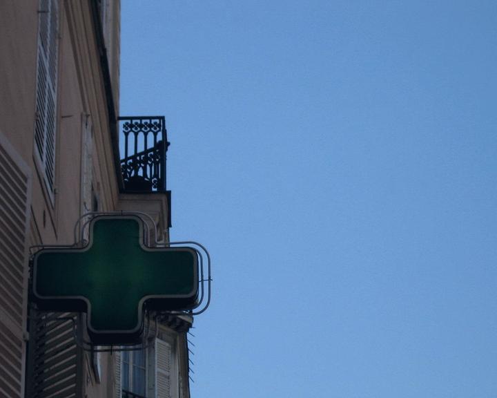 Croix de pharmacie éteinte en plein jour sur une façade d'immeuble